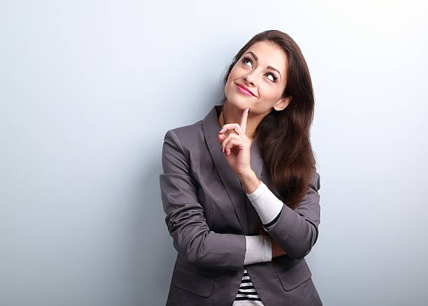 Beautiful young business woman thinking and looking up on blue background